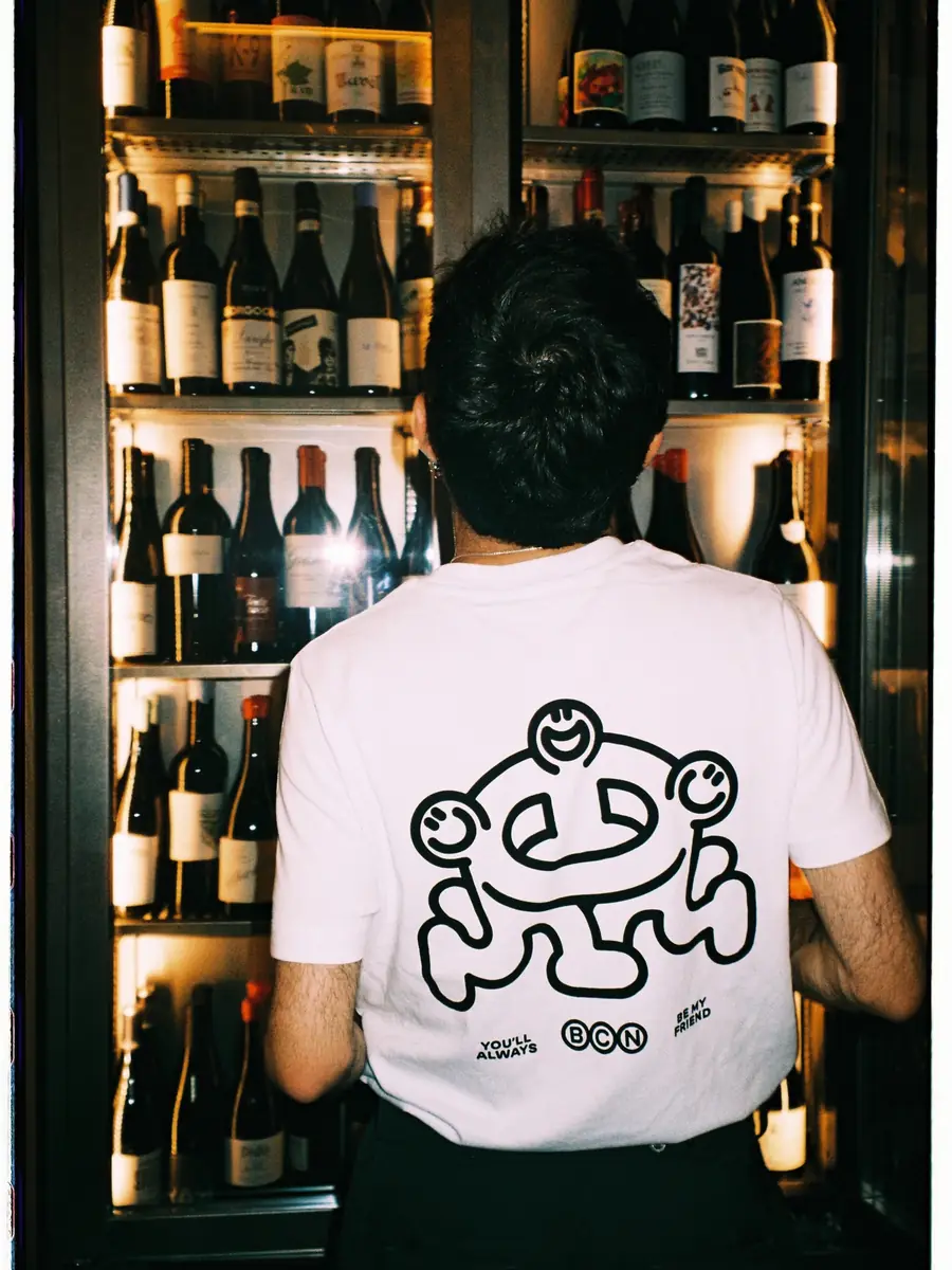 Un cambrer d’esquena, amb la mascota d’Amicks a la samarreta, davant la nevera de vins