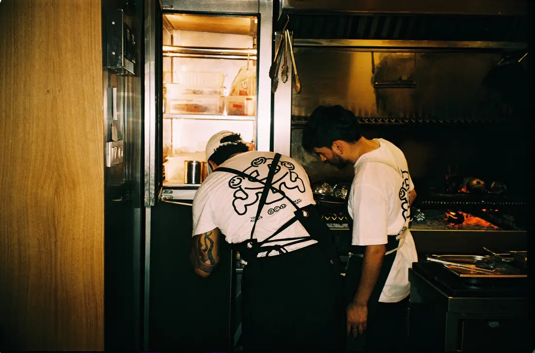 Dos cuiners treballen a la brasa de la cuina oberta