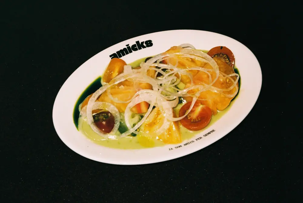 Amanida de tomàquets de temporada amb ceba, en un plat amb el logo d’Amicks