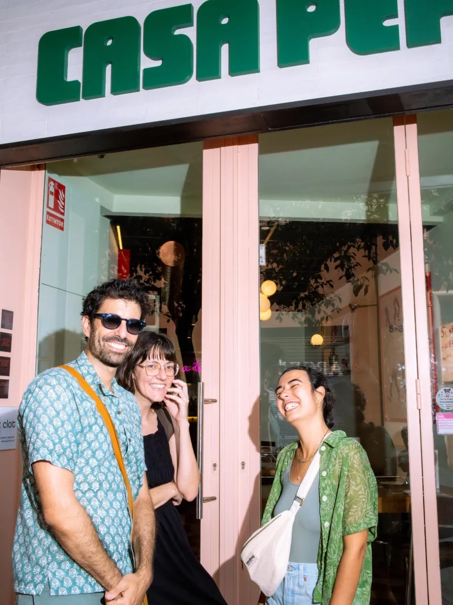 Tres clients rient a la porta de Casa Pepi, sota el rètol verd del local