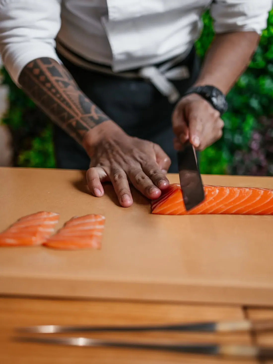 Un cocinero corta láminas de salmón en la tabla de madera