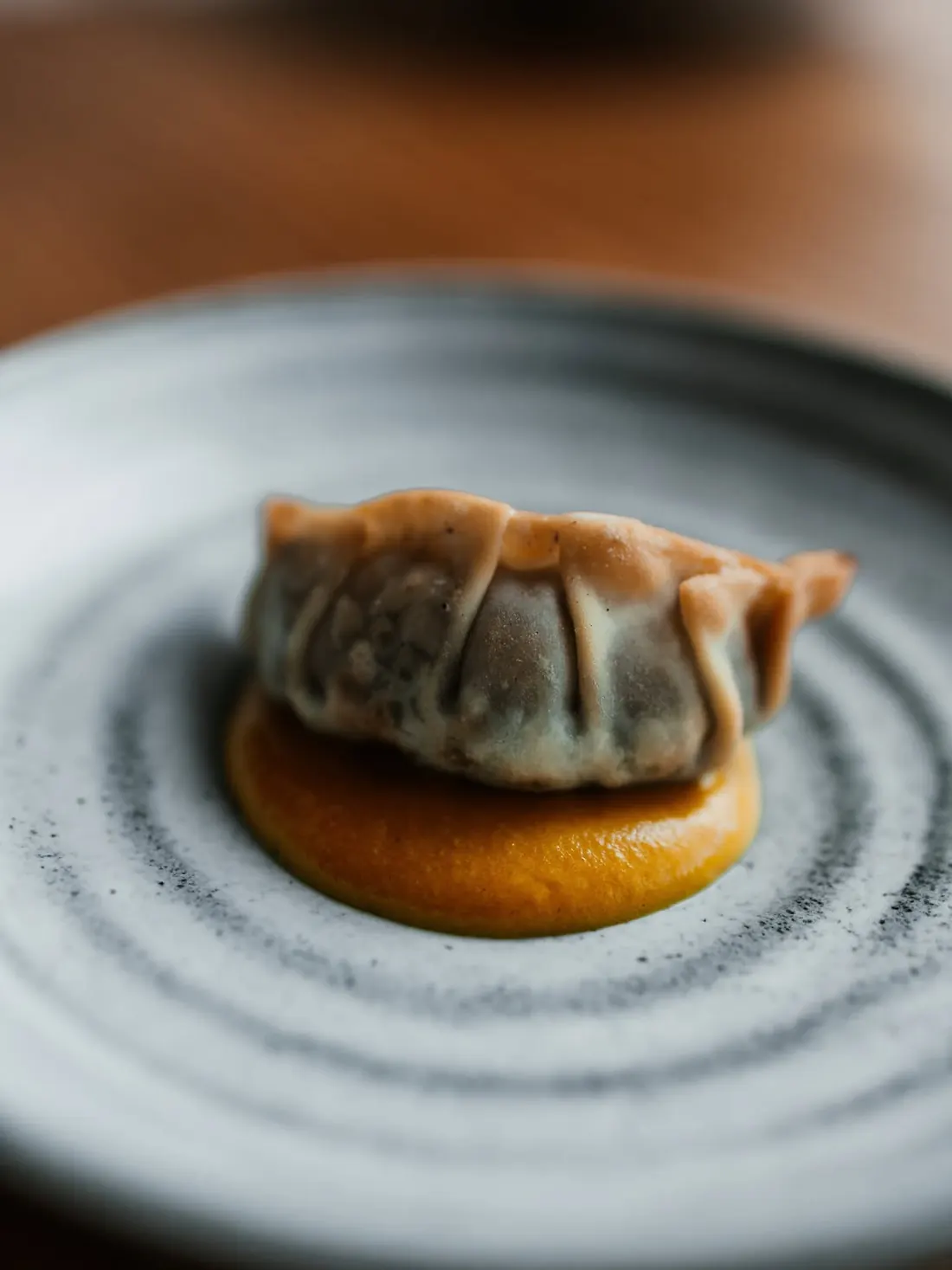 Una gyoza dorada sobre salsa amarilla en un plato gris