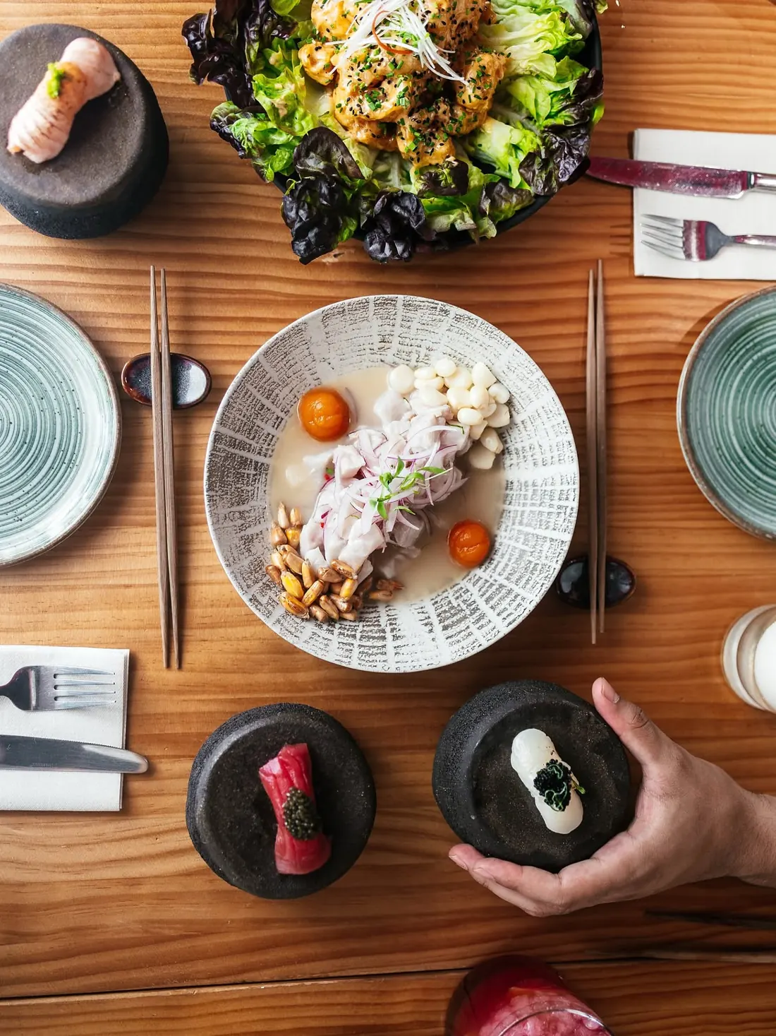 Una mesa vista desde arriba con ceviche, ensalada, nigiris y platos para compartir