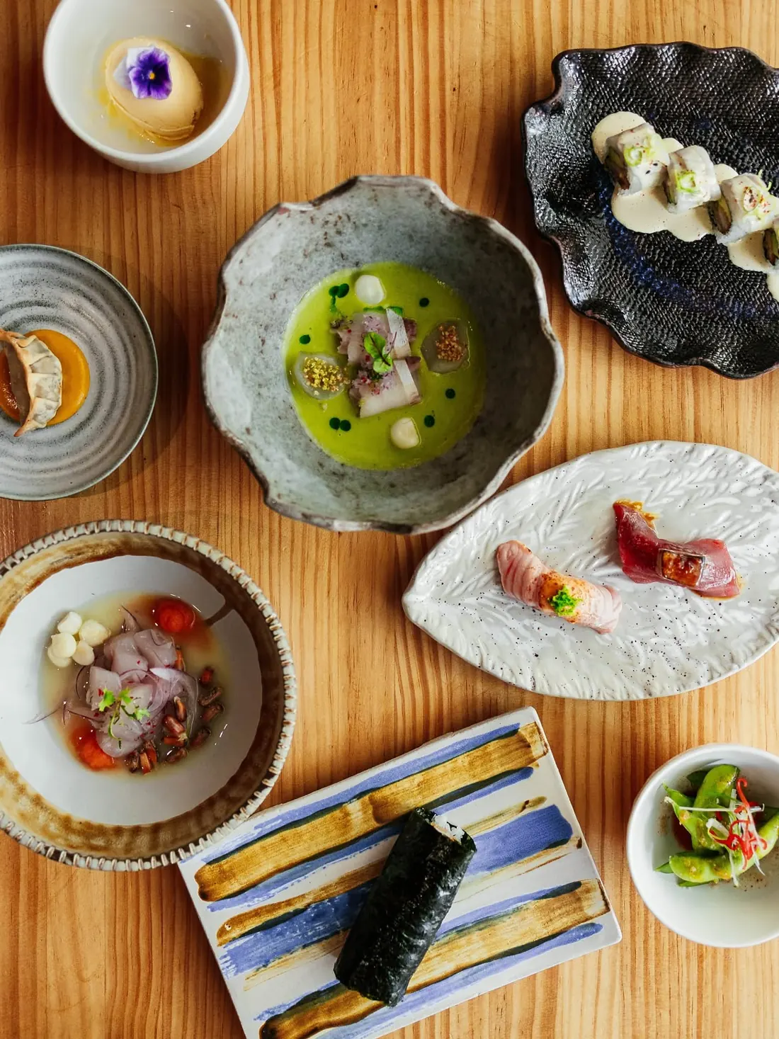 Mesa de madera vista desde arriba con tiradito, nigiris, gyoza, hand roll, ceviche y edamame