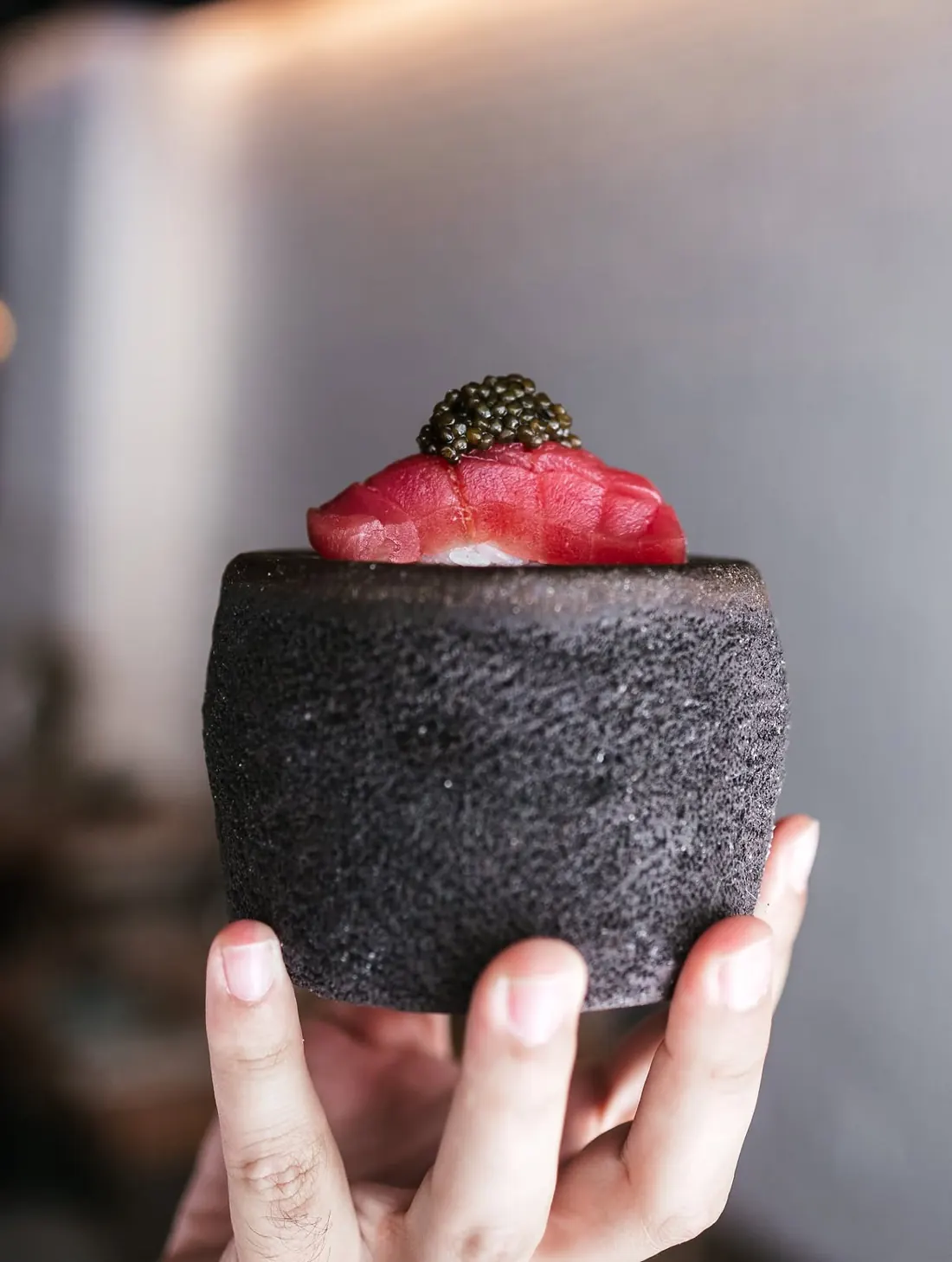 Una mano sostiene la piedra volcánica con un nigiri de atún coronado con caviar