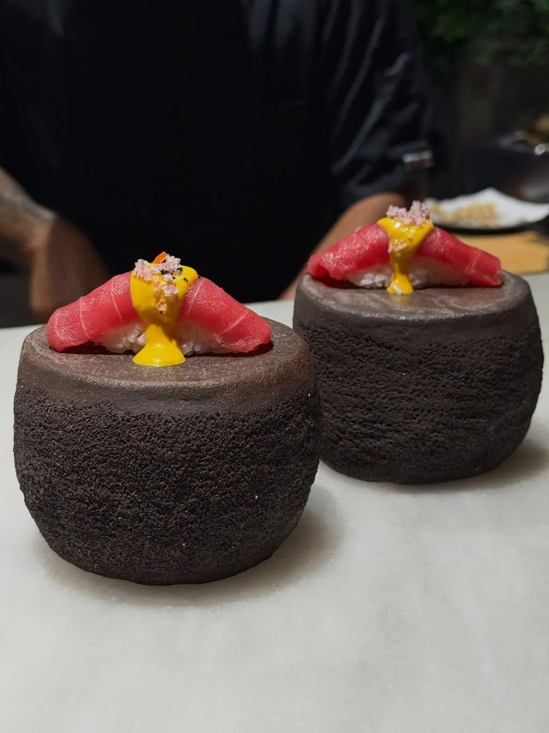 Dos nigiris de atún con salsa amarilla sobre piedras volcánicas