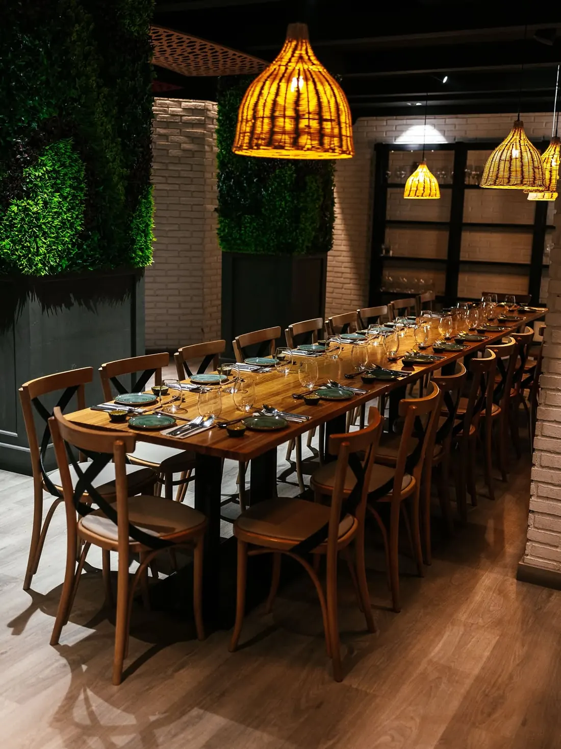 Mesa larga de madera preparada bajo lámparas de mimbre en el comedor