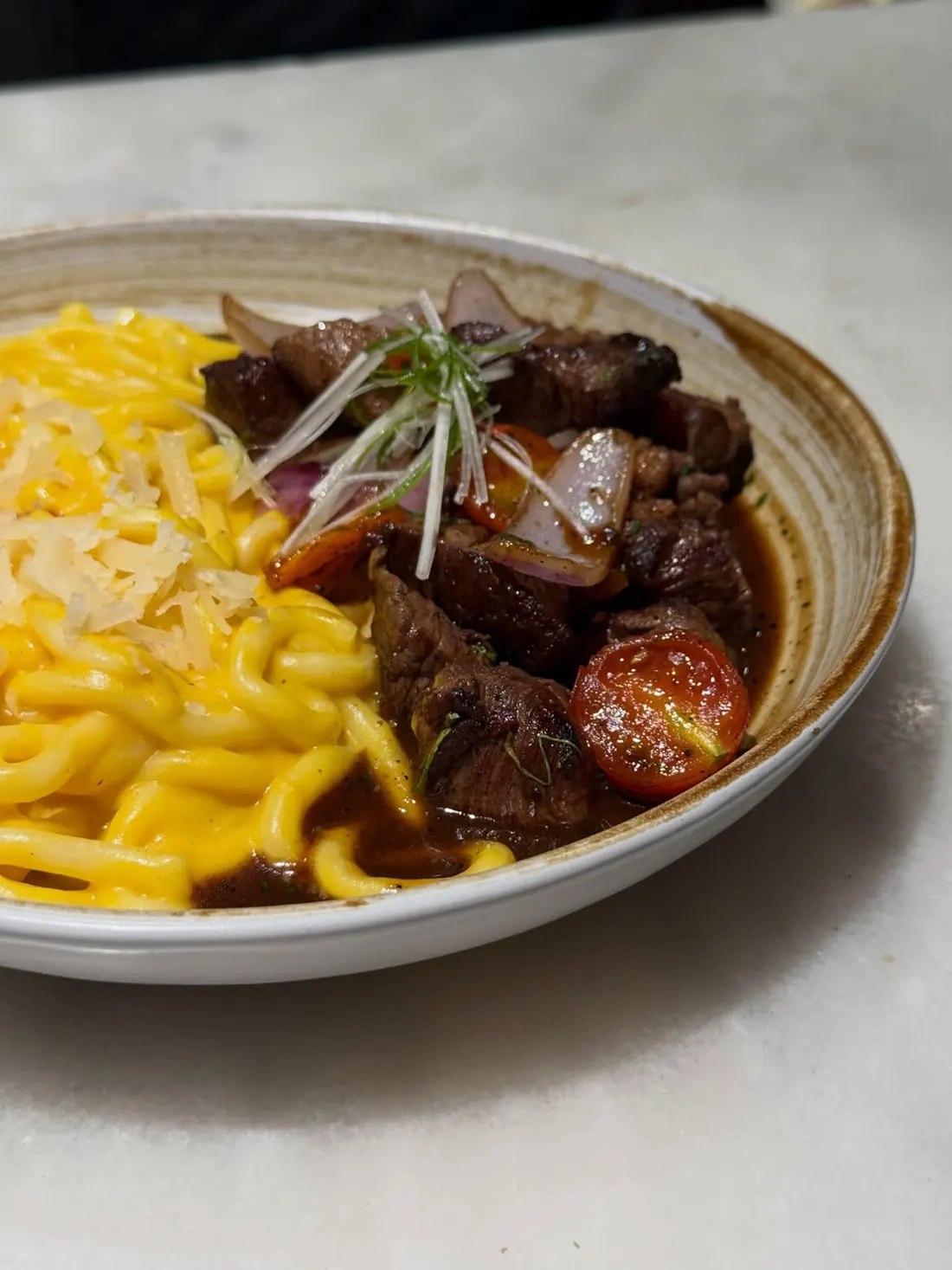 Udon amarillo en salsa huancaína junto a trozos de lomo saltado con tomate y cebolla