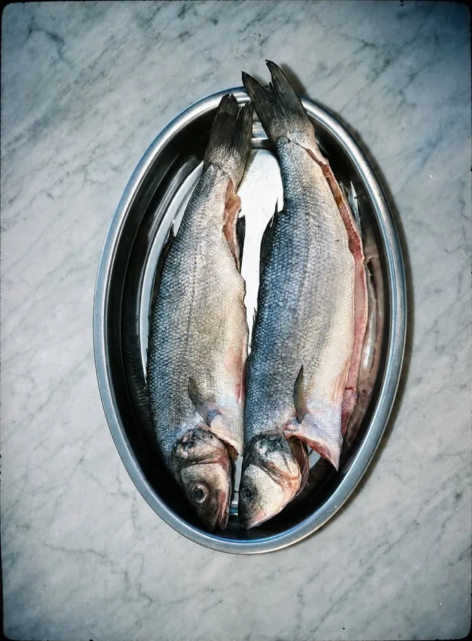 Dos pescados enteros, frescos, en una fuente sobre el mármol
