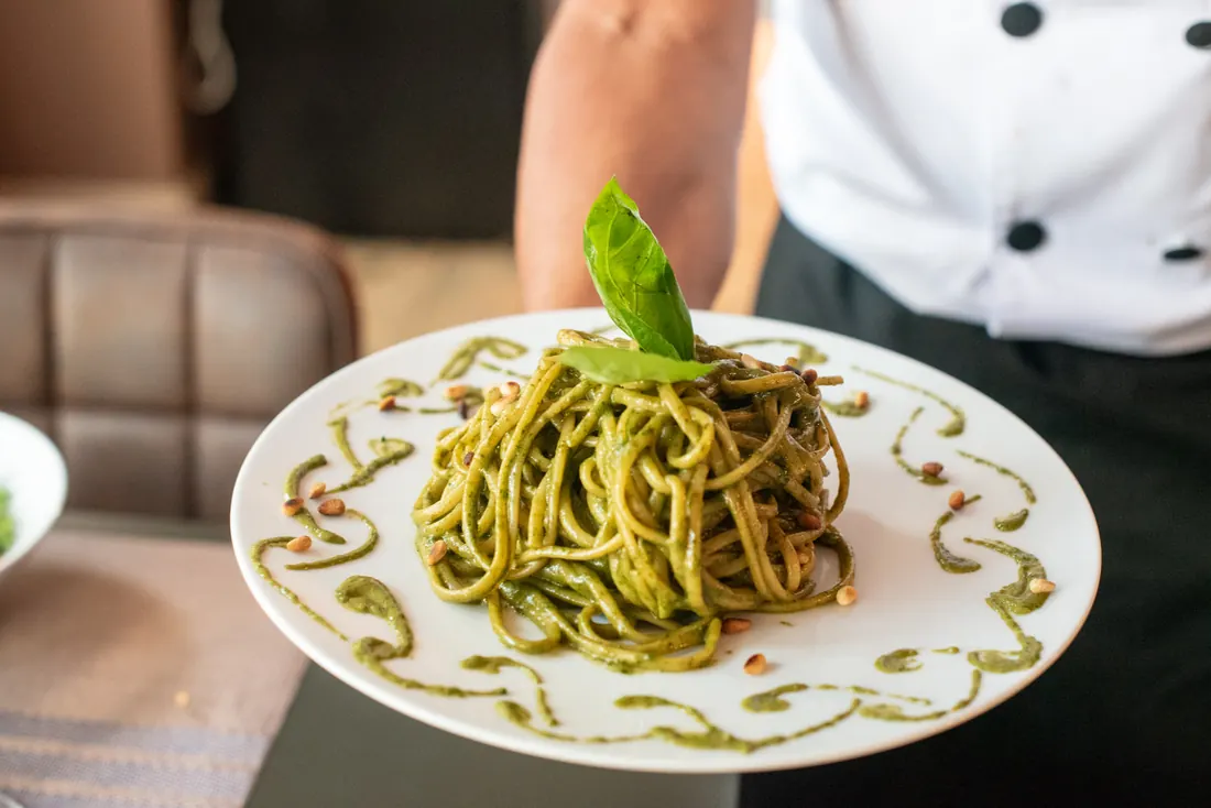 Un camarero sirve un plato de espaguetis al pesto