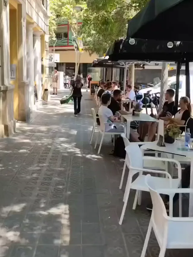 Clientes comiendo en la terraza de Via Napoli, bajo el toldo verde y los árboles de la calle Nàpols